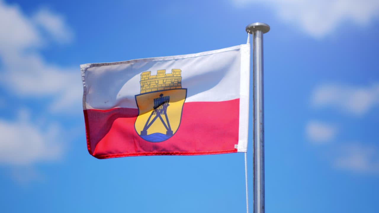 A flag of the german city Cuxhaven at the waddensea waving in the wind on asunny day. Blue sky and clouds in the background.