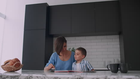 una joven madre española con su hijo sentado a la mesa enseña a leer al niño ayudando y incitando a su hijo