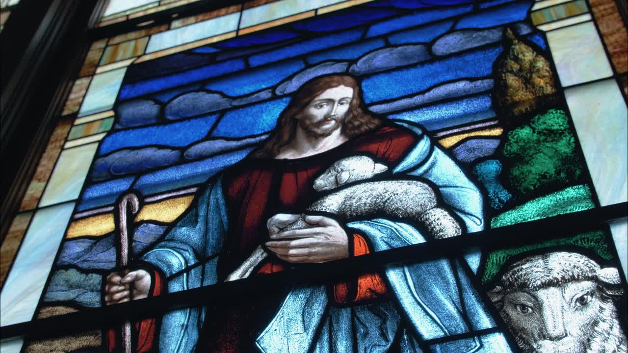 Detailní záběr okna kostela z barevného skla zobrazujícího Ježíše s ovcemi, nadčasový symbol péče, ochrany a křesťanské bohoslužby