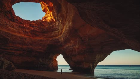 cinemagraph circuito de video sin problemas de la famosa cueva de benagil cerca de faro y lagos en el algarve, portugal con una joven modelo de mujer en un vestido de pie en la playa de vacaciones turísticas al amanecer en verano con las olas del mar moviéndose suavemente.