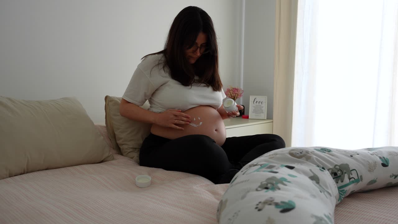 Pregnant woman on bed applying cream in the shape of a smiley face