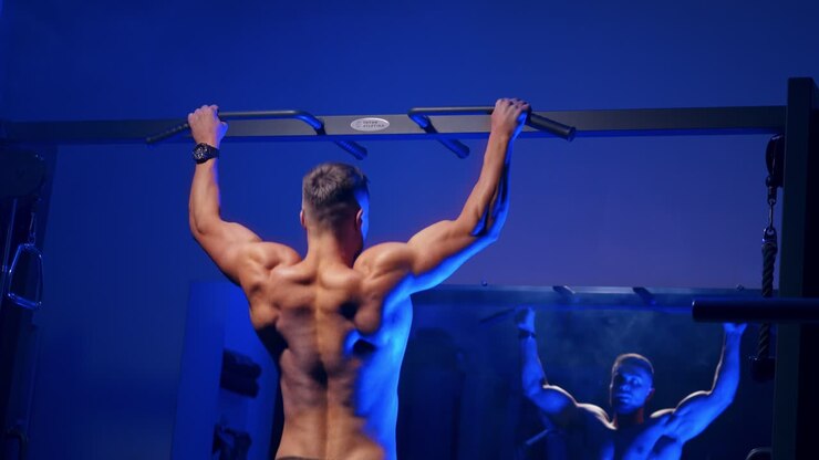 Man training on horizontal bar in gym. Back view portrait of young bodybuilder doing pull ups on the horizontal bar indoors