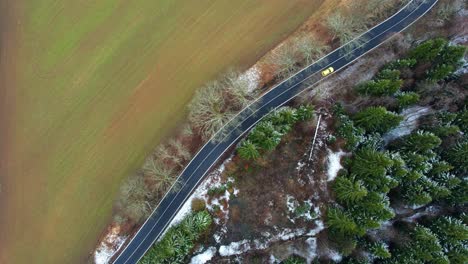 car-alone-driving-on-a-countryside-road-surrounded-by-farm-fields-and-trees---Drone-shot