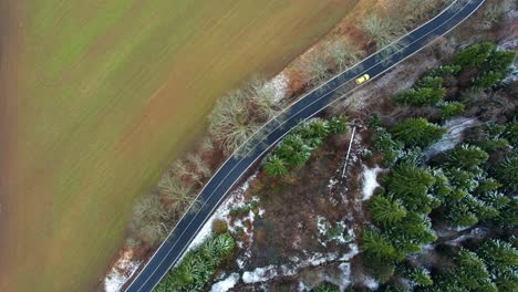 car alone driving on a countryside road surrounded by farm fields and trees - drone shot