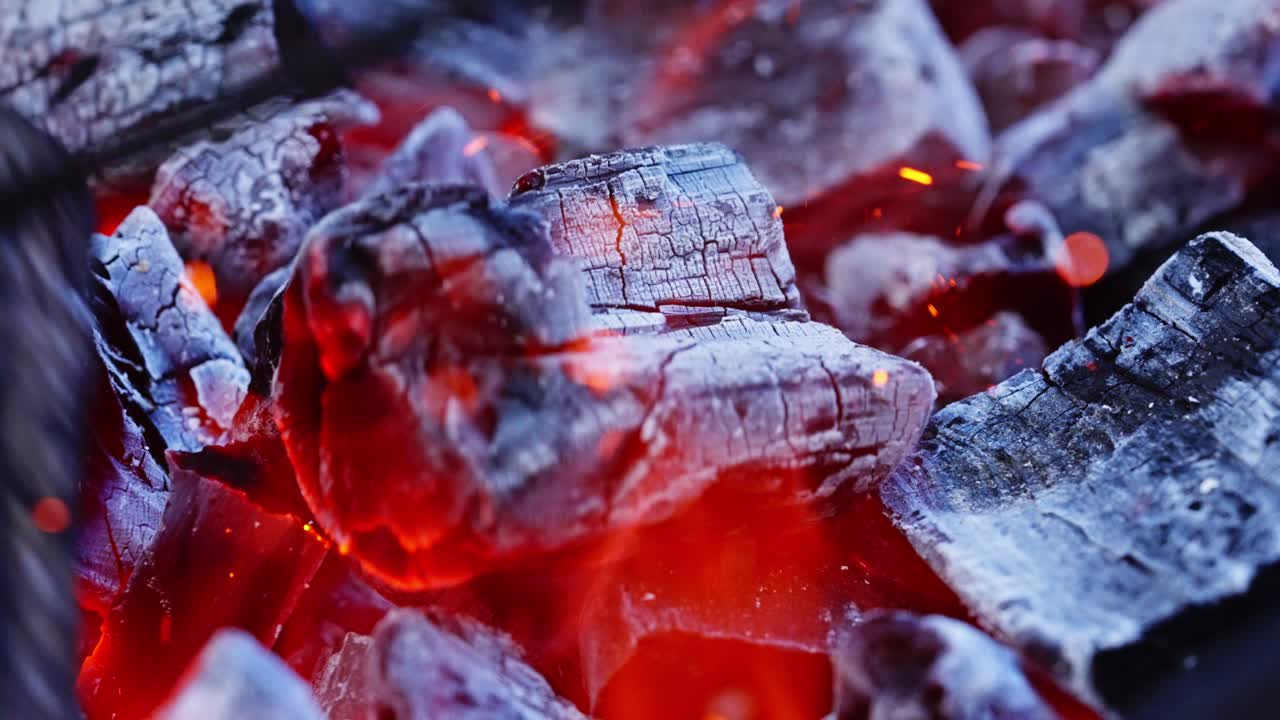 Glowing red coals burn intensely with heat and flames rising from blackened wood, backdrop background