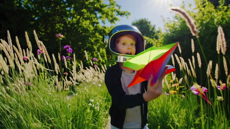 child astronaut launches colorful paper airplane in sunny field