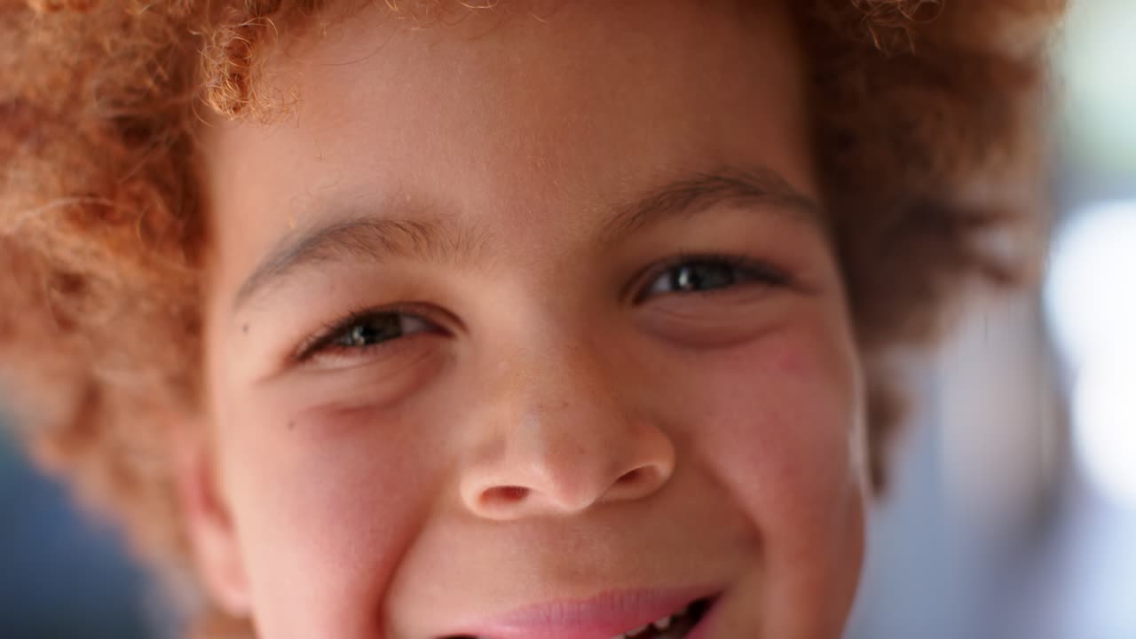 African American male child noticing camera, squinting, smiling and moving closer on shaded porch