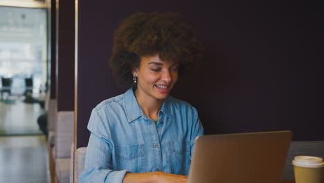 Cerca-De-Una-Mujer-De-Negocios-En-Una-Oficina-Moderna-Trabajando-En-Una-Computadora-Portátil-En-Un-Módulo-De-Asientos-Con-Una-Bebida-Para-Llevar