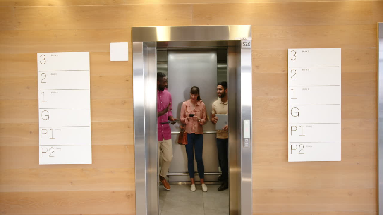 Exiting elevator, three diverse colleagues laughing and discussing work in office building