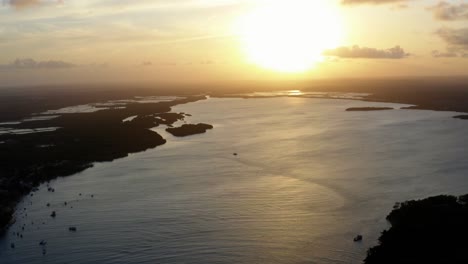 impresionante dron aéreo dejó una toma de camión de una puesta de sol dorada que se refleja en un río amazónico gigante en la ciudad de playa tropical de tibau do sol cerca de pipa en el norte de brasil en una cálida tarde de verano