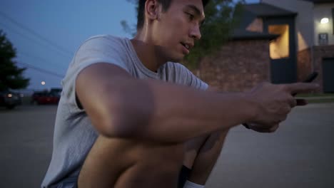 static shot of a young, asian male adult sitting down and browsing on a smartphone at outdoor parking lot