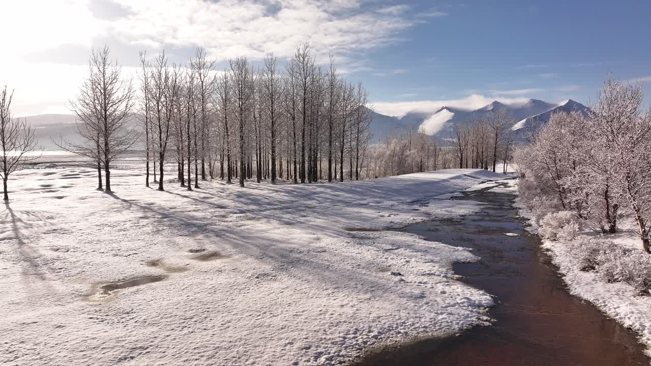 Sweeping aerial views showcase the winter landscape of Borgarfjörður, Iceland, featuring tranquil fjord waters reflecting cloudy skies and snow-capped mountains including Hafnarfjall, Kessuhorn