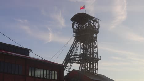 old industrial tower with a czech flag on top, standing next to a red brick building under a clear sky