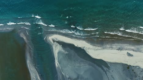 waves crash up stream of glacial delta from river with turquoise blue water on sand banks