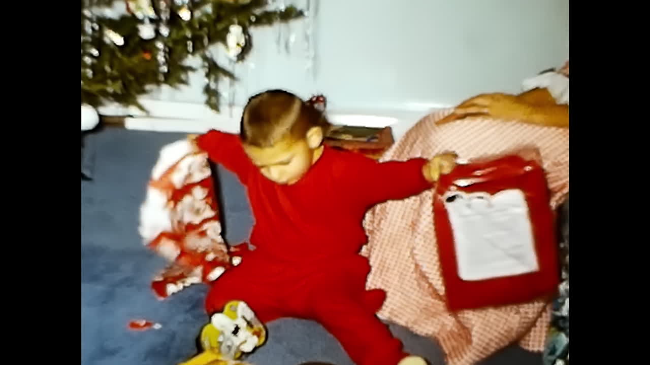 Boy Sitting Next to Christmas Tree. CIRCA USA - 1970s: A boy from the 1970s in the USA is seen sitting on the floor alongside a decorated Christmas tree.