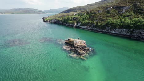 a man exploring a small rocky island with a paddleboard surrounded by turquoise sea water in a loch in the scottish highlands