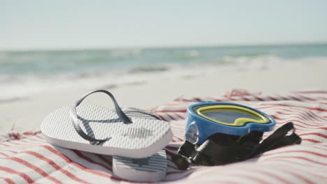 close up of goggles, flip flops and towel on beach, in slow motion, with copy space