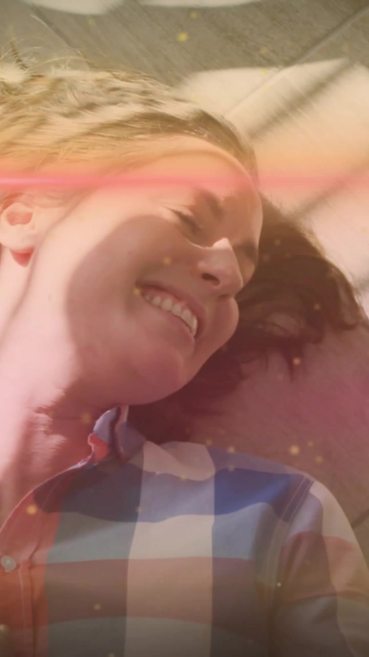 Video vertical: Mujer en un sofá reaccionando al toque de su pareja, sonriendo, con un brillo rosado en el rostro por salud