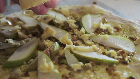 slicing cheese on to a pizza topped with pears