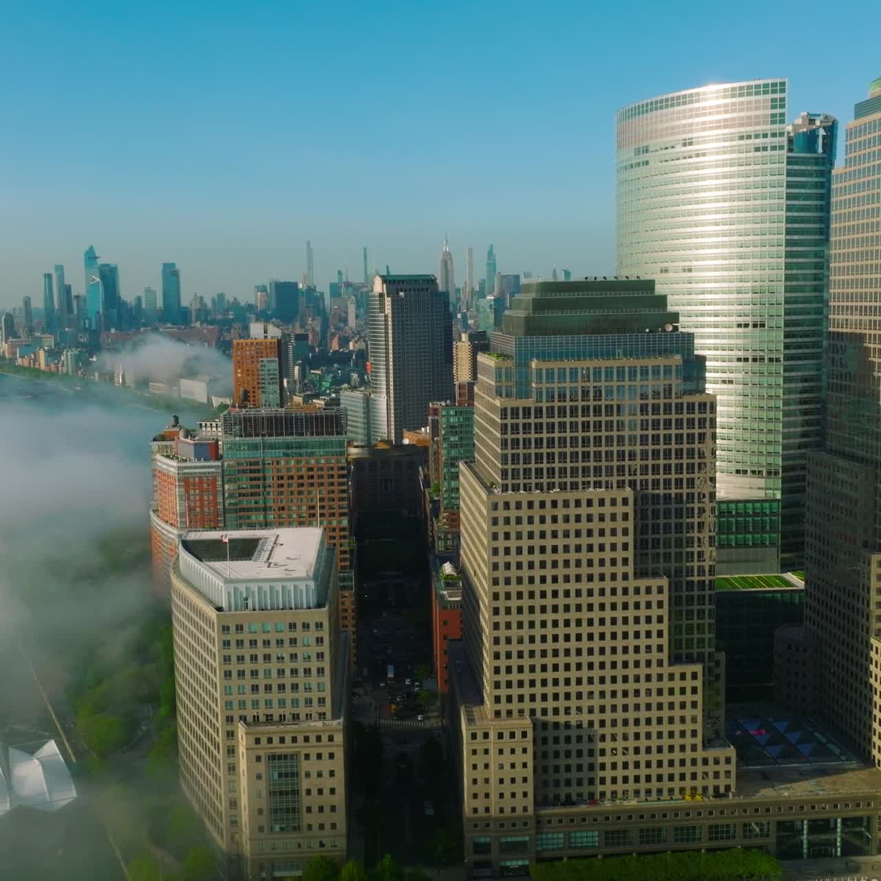 Sun rays reflecting in the windows of beautiful skyscrapers in Lower Manhattan Financial District. Tremendous New York cityscape neighboring with Hudson river covered with fog