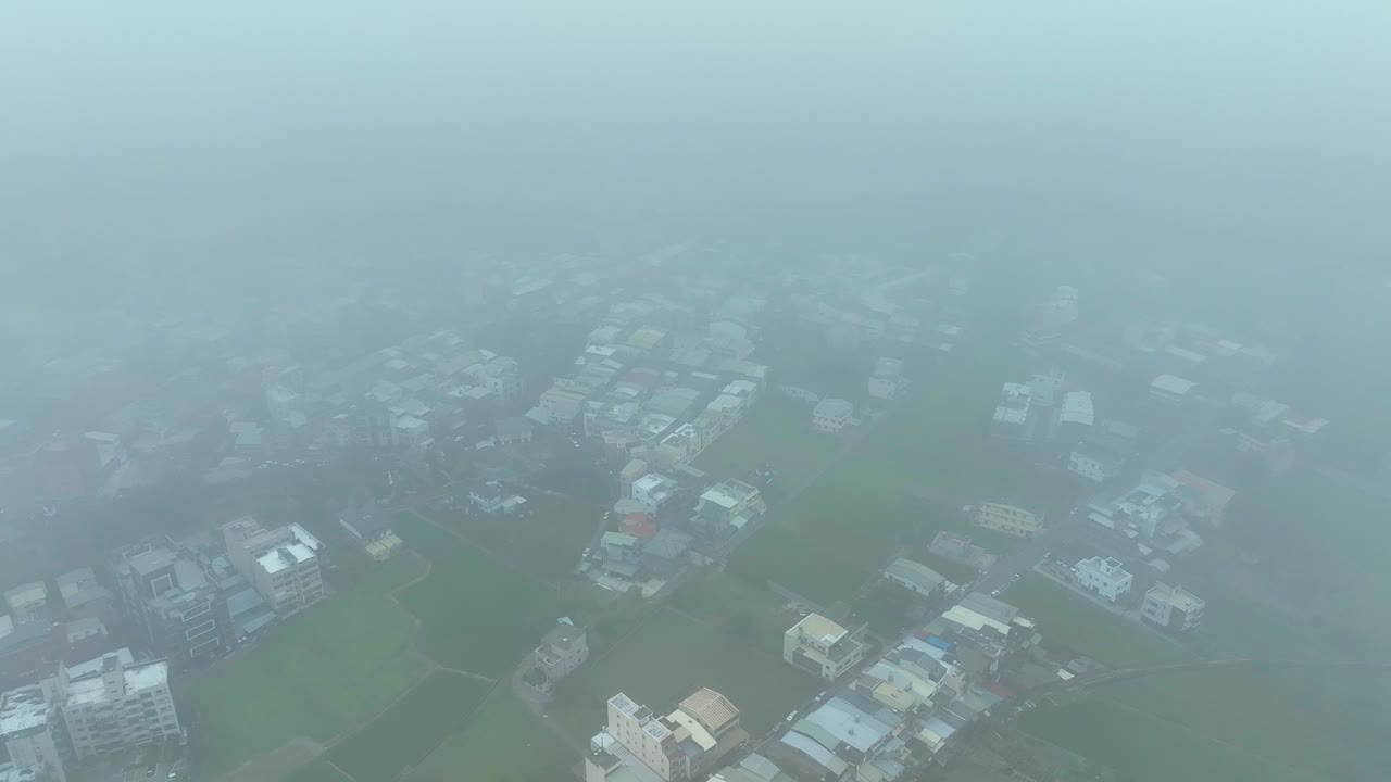 Aerial revealing shot of dense clouds and city of Miaoli with green fields in Taiwan