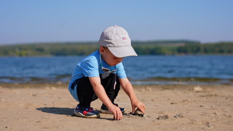 cute baby boy runs up to a stone lying on the sand. kid picks up rocks on the beach and goes to water.