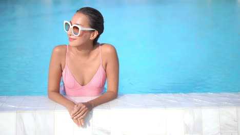 Mujer-Asiática-Sexy-En-Traje-De-Baño-En-La-Piscina-Mirando-Alrededor-Y-A-La-Cámara-Con-Una-Sonrisa