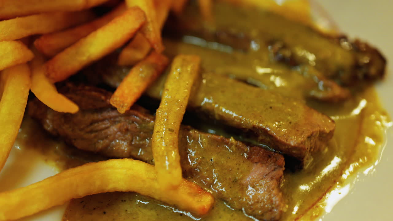 Close up of a plate of fries with meat and green sauce on a plate