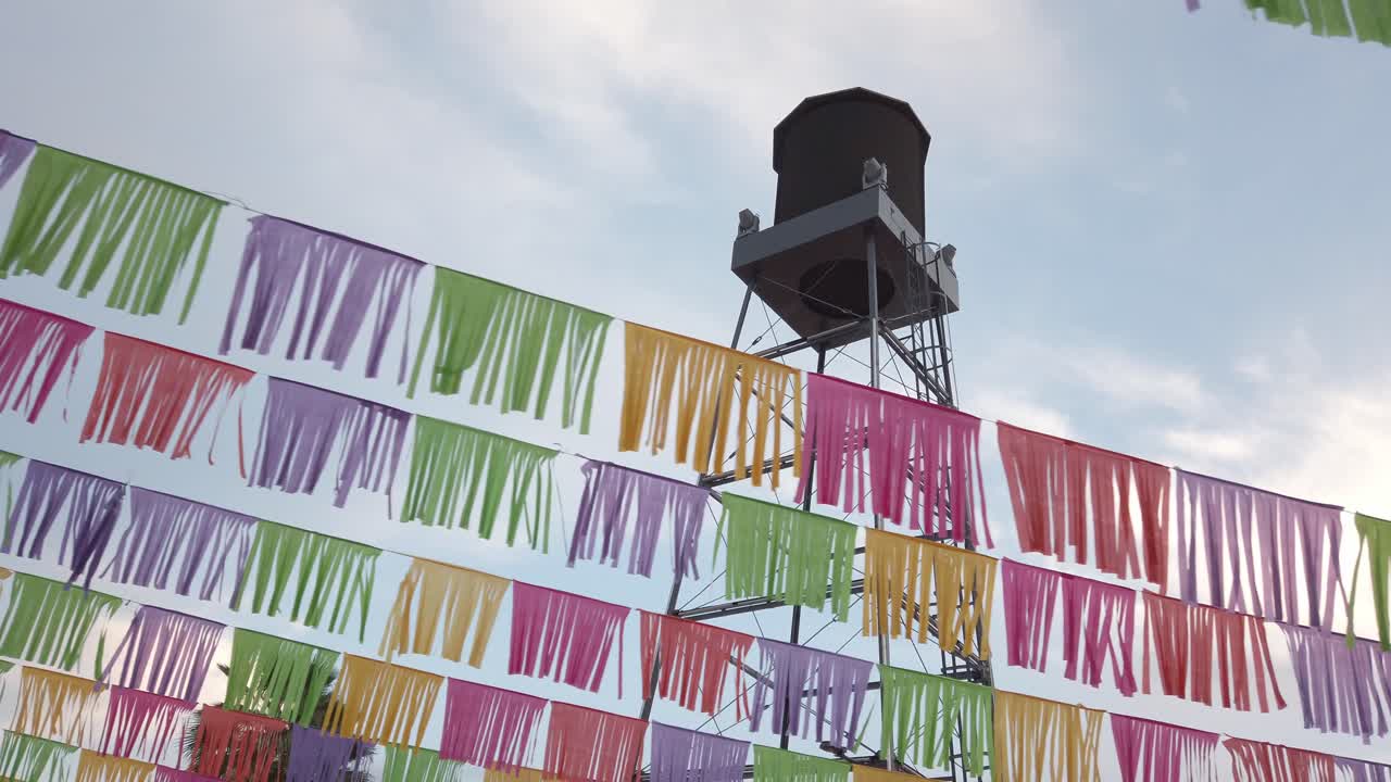 Smooth pan right showing decorative colored paper streamers hanging across sky with water tank in background