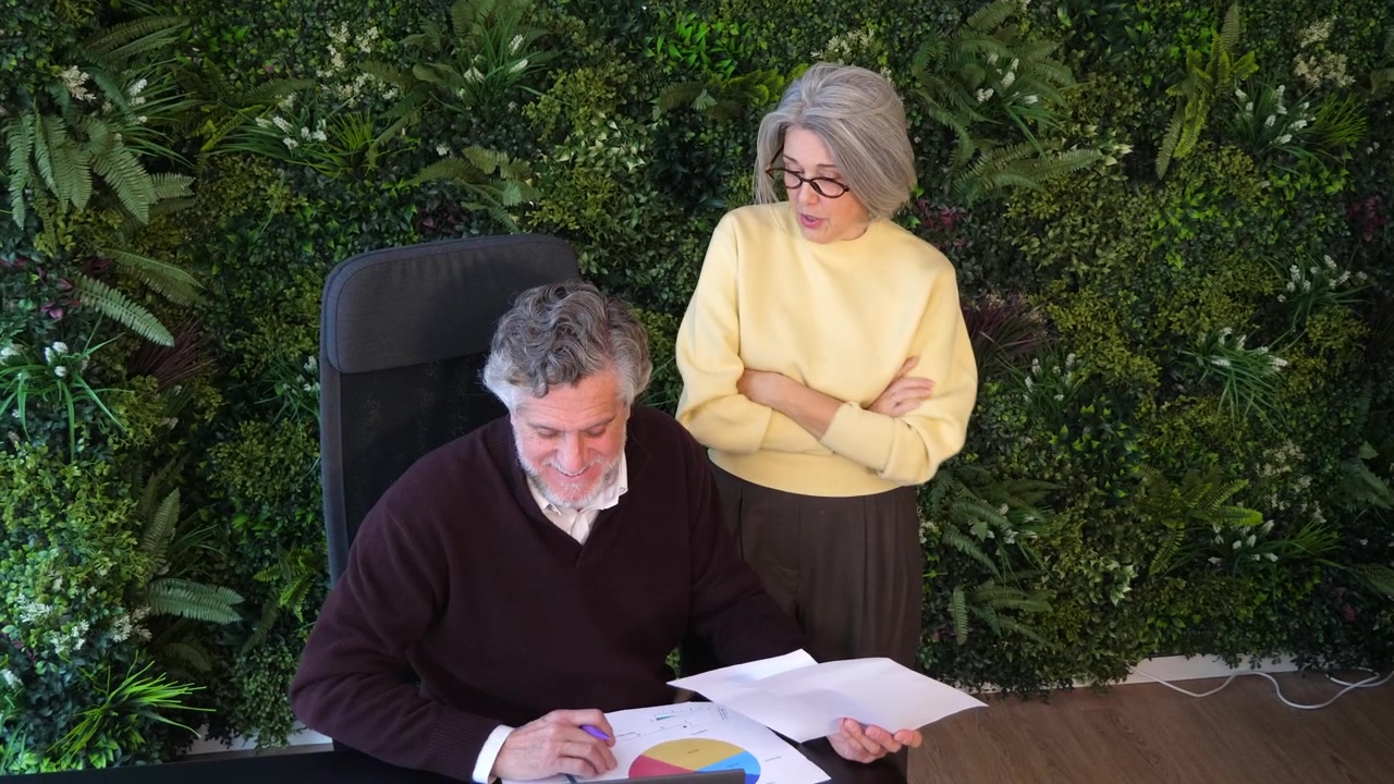 Plano de ângulo alto de executivo sênior à mesa revisando relatórios em papel enquanto colega de pé observa. Conceito para auditoria de escritório, revisão financeira, trabalho em equipe e gestão