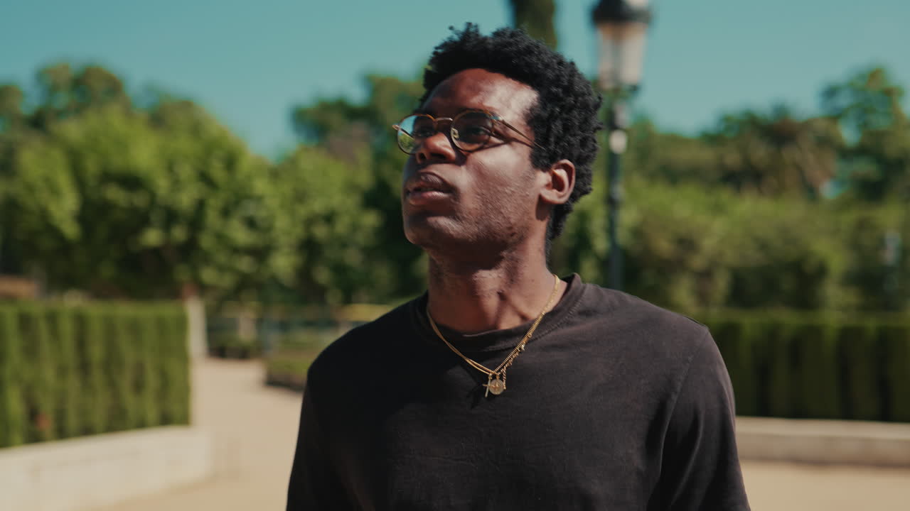 Joven negro caminando y mirando a su alrededor en un parque soleado