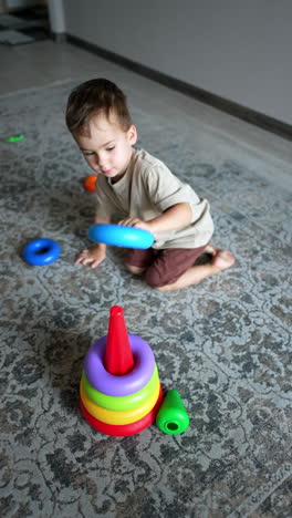little toddler boy quickly builds a colorful toy pyramid. kid plays with a toy on the floor. top view. vertical video.