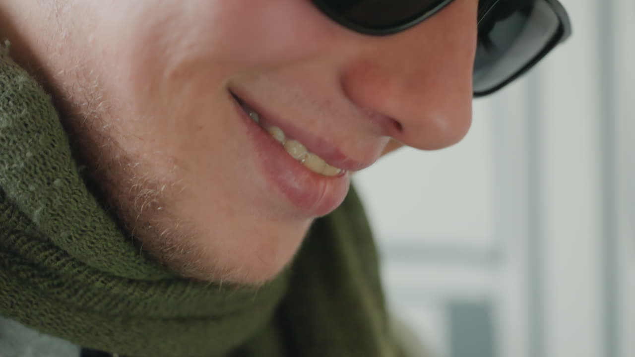 Close up white man wearing sunglasses captured indoors with green scarf, subtle stubble and soft smile candid sequence shows gentle downward gaze and shifting expressions, warm natural light, relaxed