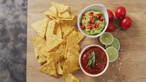 Close-up-of-nachos-and-sauces-on-wooden-tray-on-black-surface