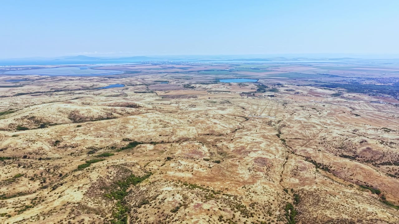 Ampia vista di paesaggio arido con montagne distanti e specchi d'acqua sotto un cielo azzurro e limpido