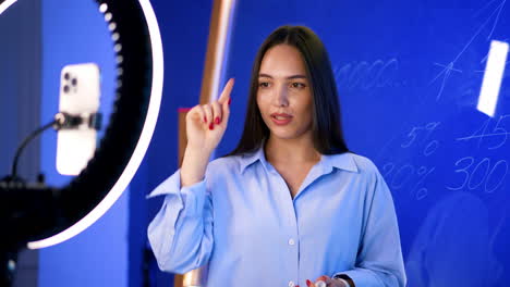 brunette lady talks to camera with light ring. woman demonstrates numbers on the glass wall.