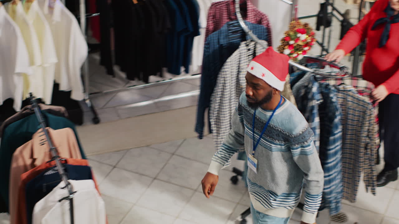 empleados con sombreros de santa y clientes caminando a través de la tienda de ropa decorada con navidad durante la temporada festiva. trabajadores y clientes en la tienda de moda adornada con xmas
