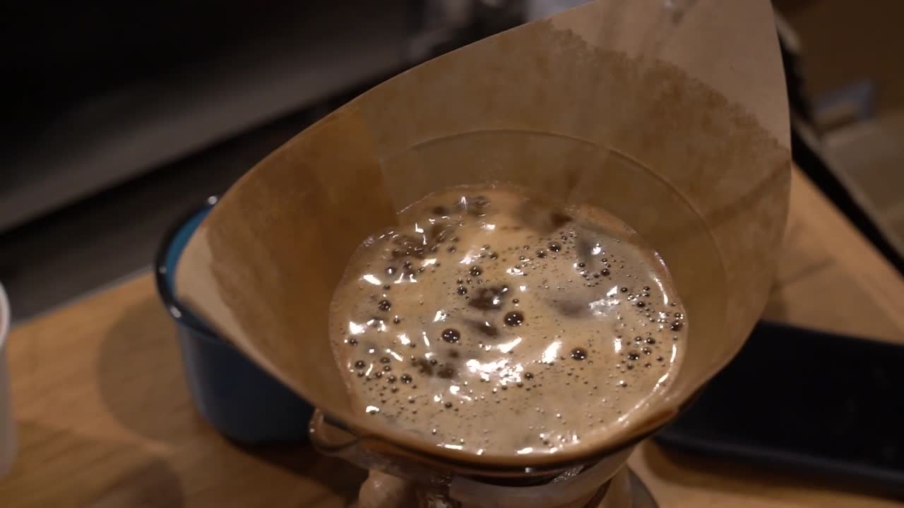 Coffee filter with fresh crushed grains being filled with hot water for creating a brewed cup, Close up handheld shot