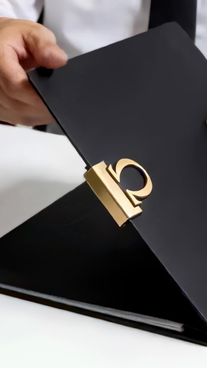 Vertical video: Gripping folio, man in white shirt and black tie showing gold clasp on white table