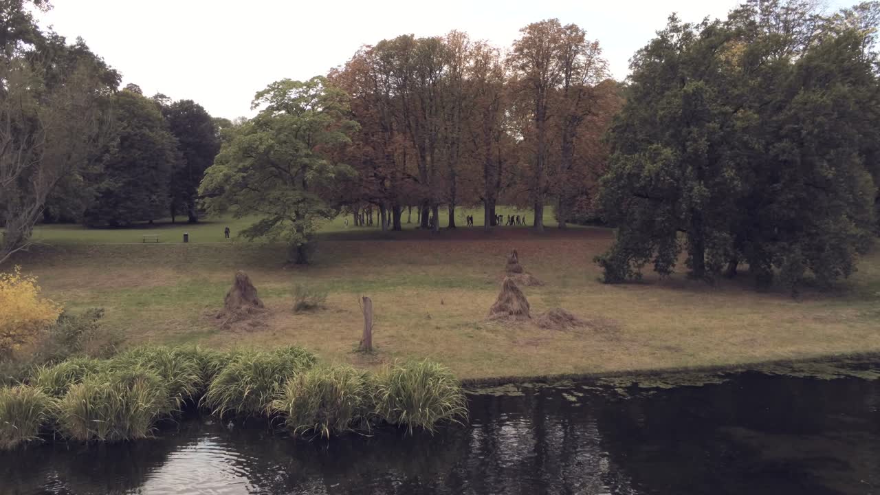 siluetas de escolares caminando detrás de los árboles de otoño cerca de un lago reflectante en un hermoso parque