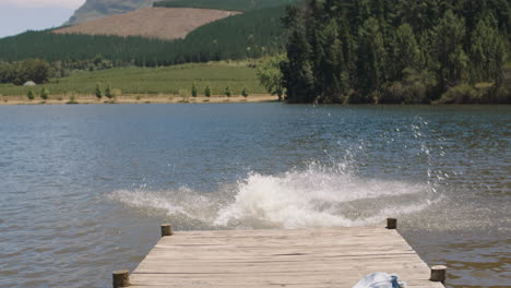 happy couple running jumping off jetty in lake splashing in water having fun summer vacation