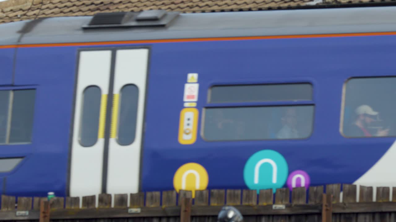 Modern passenger train travels past brick wall, daytime, side view, clear weather, urban environment