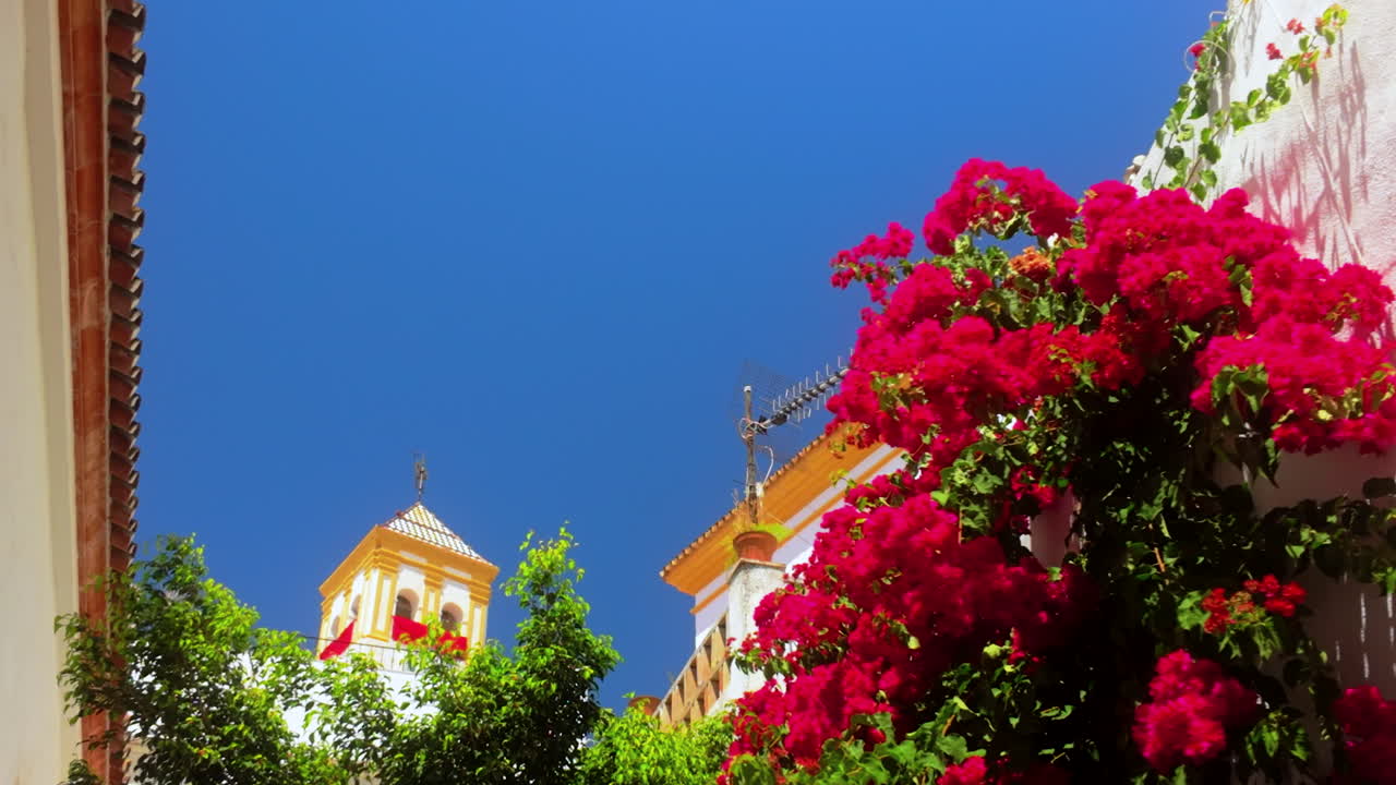 Beautiful courtyard in Marbella, Spain, featuring a church tower in the background with blooming red bougainvillea against a clear blue sky