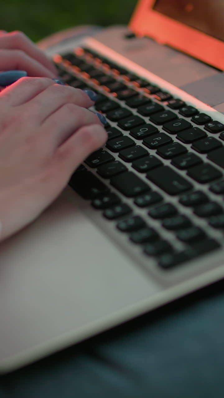 Close-up of woman typing on laptop with well-polished nails, sunlight reflecting on the keyboard, soft bokeh light effect in the background