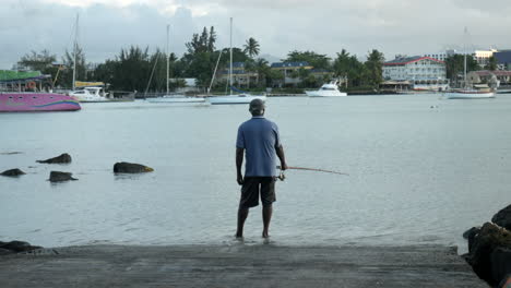 toma trasera de un pescador mauriciano pescando en la orilla del puerto, estático