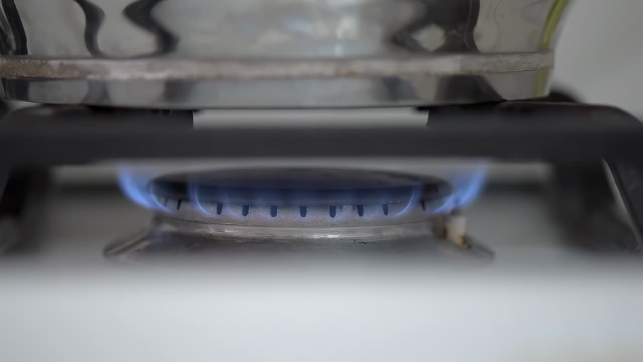 Close up of a blue flame at the burner of a stove heating a pot