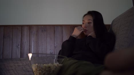 young asian woman sitting on sofa and eating popcorn