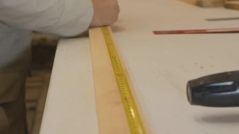 the girl carpenter measures the distance necessary to cut the board with a tape measure. the color of her nails is similar to the color of a tape measure. women's work as a joiner. 4k