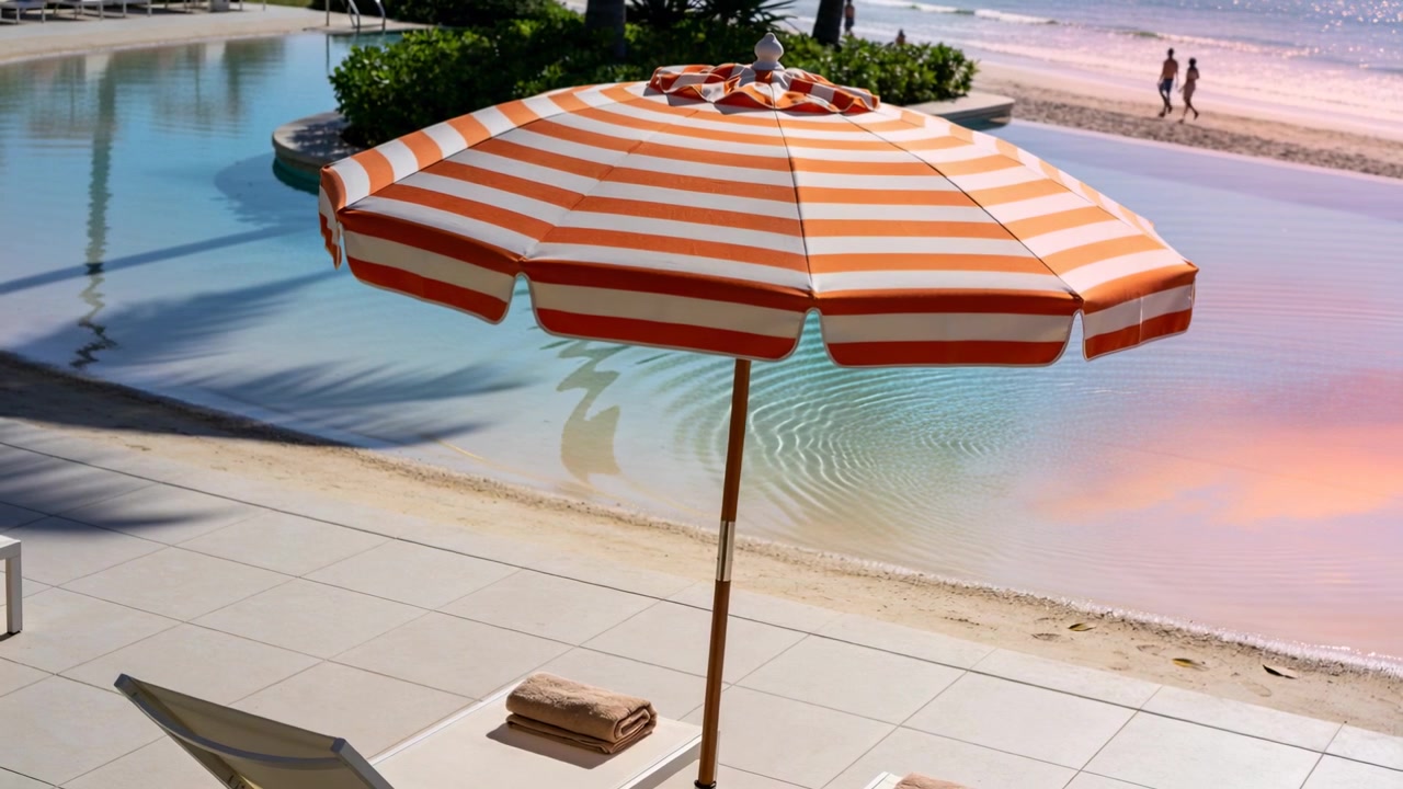 Inquadrando un ombrellone a strisce che ombreggia il bordo piscina, la brezza crea increspature, coppia che cammina sulla riva in costume da bagno