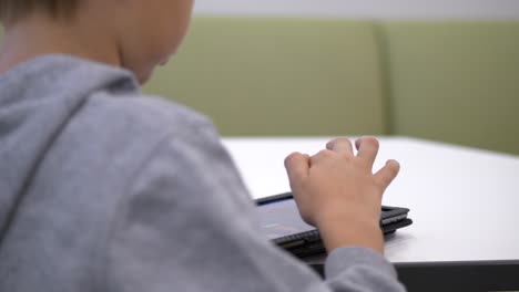 Close-up-behind-blond-boy-reading-on-tablet,-Static